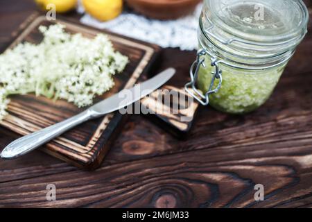 Zerkleinern von Zitrone und schwarzer Holunderbeere auf einem Schneidebrett zur Herstellung eines Kräutergetränks oder eines Medikaments zur Heilung von Sirup aus Holunderblüten zu Hause. Stockfoto