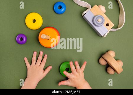 Nahaufnahme eines kleinen Babys im Pyjama, das mit der Holzpyramide auf grünem Hintergrund spielt. Natürliches umweltfreundliches Spielzeugkonzept. Stockfoto