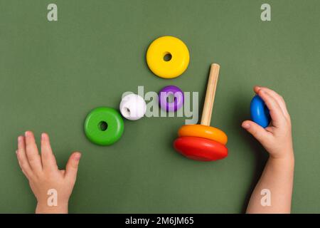 Nahaufnahme eines kleinen Babys im Pyjama, das mit der Holzpyramide auf grünem Hintergrund spielt. Natürliches umweltfreundliches Spielzeugkonzept. Stockfoto