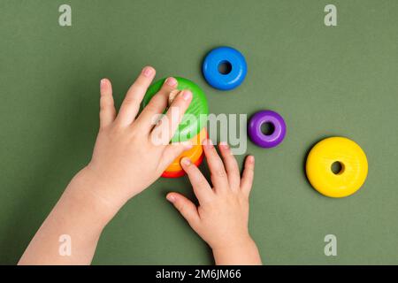 Nahaufnahme eines kleinen Babys im Pyjama, das mit der Holzpyramide auf grünem Hintergrund spielt. Natürliches umweltfreundliches Spielzeugkonzept. Stockfoto