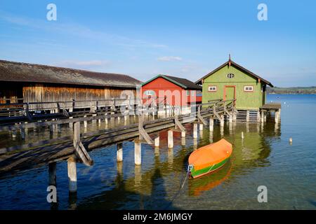 Ein langer hölzerner Pier, der zu den farbenfrohen Bootshäusern am Ammersee im deutschen Fischerdorf Schondorf führt (Ammersee, Deutschland) Stockfoto