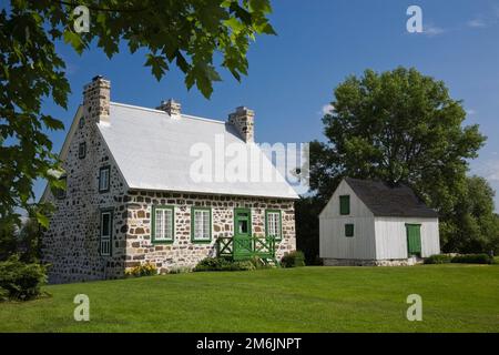 Altes 1785 Feldsteinhaus im Landhausstil mit grüner Verkleidung und kleiner weißer Scheune im Sommer. Stockfoto