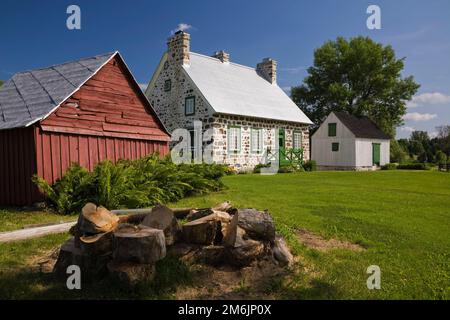 Altes 1785 Feldsteinhaus im Landhausstil mit grünen Zierleisten und kleinen Scheunen im Sommer. Stockfoto