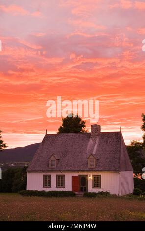 Altes Haus im Stil eines französischen Regimes aus dem Jahr 1752, beleuchtet in der Abenddämmerung im Sommer, Saint-Francois, Ile d'Orleans, Quebec, Kanada. Stockfoto