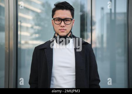 Ein asiatischer Geschäftsmann mit Kopfhörern, mitten im Bild, draußen Stockfoto