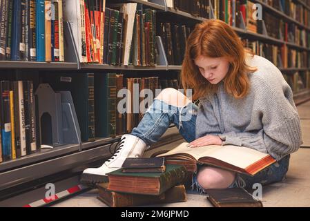 Teenager, die auf dem Boden sitzt und in der Bibliothek liest. Stockfoto