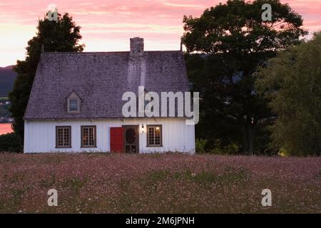 Altes Haus im Stil eines französischen Regimes aus dem Jahr 1752, beleuchtet in der Abenddämmerung im Sommer, Saint-Francois, Ile d'Orleans, Quebec, Kanada. Stockfoto