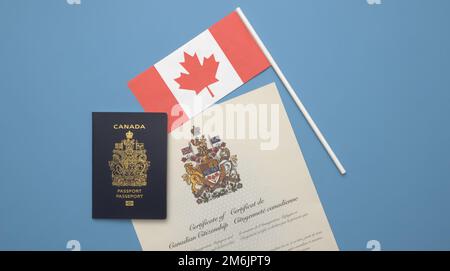 Ein kanadischer Reisepass auf kanadischer Flagge und ein kanadisches Staatsbürgerschaftszertifikat vor einem leuchtend hellblauen Hintergrund Stockfoto