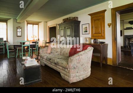 Gepolstertes Sofa, alter antiker Holzkistentisch im Wohnzimmer und brauner ovaler Holztisch mit grünen Stühlen im Esszimmer im alten Haus. Stockfoto