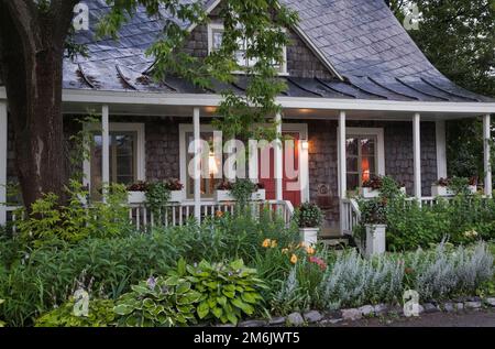 Alte verwitterte Zedernschindeln aus den 1809 Jahren mit weißer Innenfassade im Landhausstil in der Dämmerung im Sommer, Saint-Laurent, Ile d'Orleans, Quebec, Kanada. Stockfoto