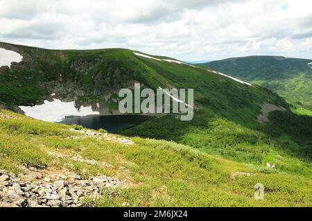 Ein kleiner See in einer Höhen-Höhle mit den Überresten von Schnee auf den Hängen, die mit Gras überwuchert sind. Iwanowskie-Seen, Chakassien, Sibirien, Russland. Stockfoto