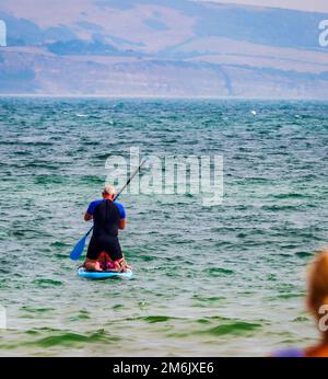 Ein Mann sitzt und benutzt ein Paddelbrett in Weymouth Beach in Dorset England Stockfoto