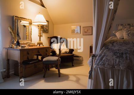 Antike Holzkommode mit gepolstertem Stuhl und Doppelbett Himmelbett im Schlafzimmer im oberen Stockwerk in einem alten Haus im Landhausstil von 1809. Stockfoto