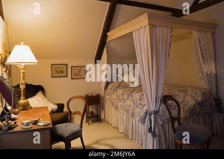 Antike Holzkommode mit gepolstertem Stuhl und Doppelbett Himmelbett im Schlafzimmer im oberen Stockwerk in einem alten Haus im Landhausstil von 1809. Stockfoto