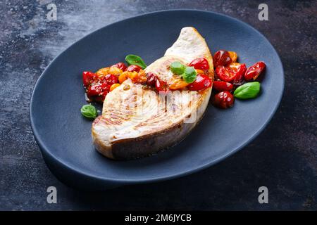 Gebratenes Schwertfischsteak mit Tomaten und Paprika, serviert aus nächster Nähe auf einem Design-Teller Stockfoto