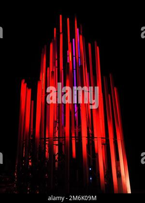 Eine leuchtend rote Leuchtanlage beleuchtet den Park bei Nacht. Längliche Lampen, die in einem Kreis in dekorativer Form gefaltet sind Stockfoto