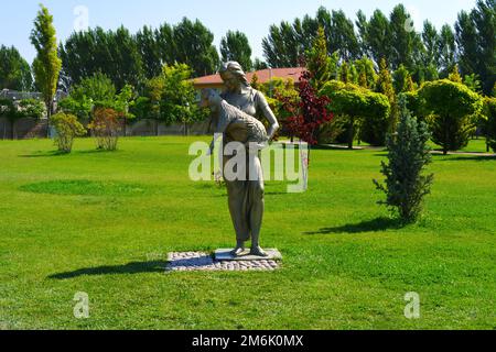 Statue einer Frau, die an einem sonnigen Tag im Park in Bäumen Lamm an den Händen hält Stockfoto