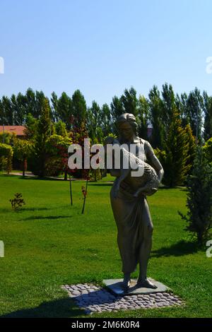 Statue einer Frau, die an einem sonnigen Tag im Park in Bäumen Lamm an den Händen hält Stockfoto