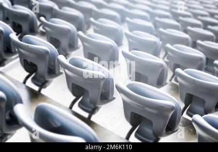 Leere graue Stühle in einem Stadion. Kunststoffsitze in Reihen. Wiederholung und Symmetrie. Stockfoto