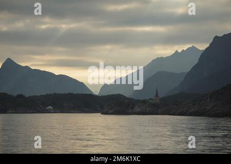 Norwegische Küste, felsige Küste mit dramatischem Himmel, die Sonne bricht durch die Wolken, schiere Klippen, kleine Inseln beleuchtet Stockfoto