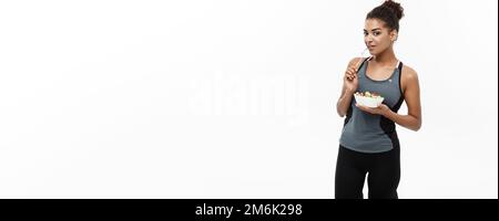 Healthy and Fitness-Konzept - Schöne Amerikanerin in Fitnesskleidung auf der Ernährung frischen Salat essen. Isoliert auf weißem B. Stockfoto