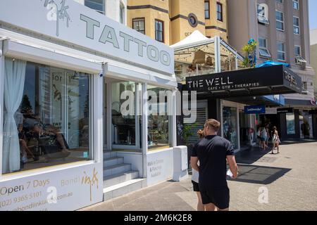 Bondi Ink Tattoo Salon und der Brunnen Gym und Cafe, campbell Parade, Bondi Beach. Ein Mann am Telefon, während er tätowiert wurde, Sydney, NSW, Australien Stockfoto