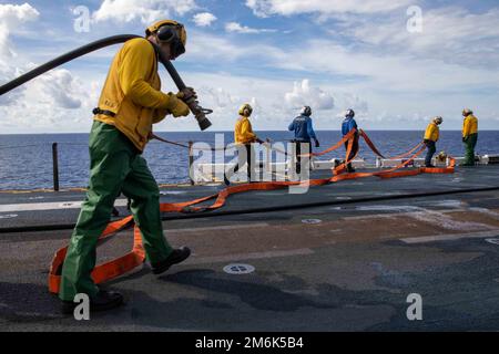 Das Celebes-Meer. 9. Dezember 2022. Matrosen verstauen Schläuche während einer Generalbohrer-Übung an Bord des Amphibienschiffs USS Makin Island (LHD 8), Dezember. 9, 2022. Sowohl im Hafen als auch auf dem Weg werden Übungen zur Schadensbegrenzung eingesetzt, um sicherzustellen, dass die Seeleute über eine angemessene Ausbildung zur Bekämpfung etwaiger Unfälle verfügen. Die Makin Island Amphibious Ready Group, bestehend aus dem Amphibienschiff USS Makin Island (LHD 8) und dem Amphibienschiff USS Anchorage (LPD 23) und der USS John P. Murtha (LPD 26), ist im US-Flottengebiet 7. tätig, mit der in Betrieb genommenen Marine Expeditionary Unit 13. Stockfoto