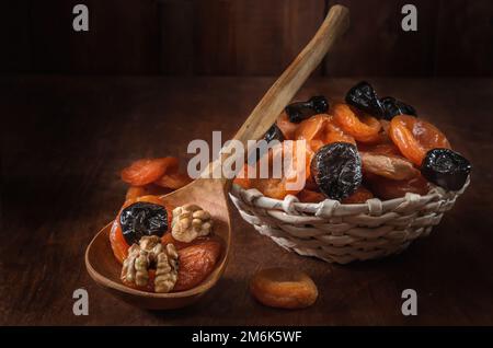 Getrocknete Aprikosen in einem Korb und andere getrocknete Früchte auf dunklem Holzhintergrund Stockfoto