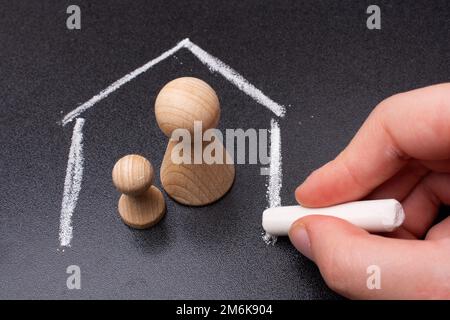 Familien- und Versicherungskonzept. Hölzerne Figuren in einem von Kreide gezeichneten Haus Stockfoto