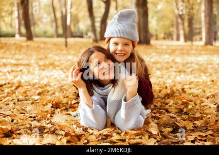 Porträt einer erstaunlichen Familie von jungen Frauen und Mädchen im Teenageralter, die im Herbst auf gelben gefallenen Blättern im Waldpark liegen. Liebe. Stockfoto