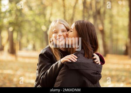 Porträt einer Familie junger Frauen und Mädchen im Teenageralter, die im Wald spazieren. Mutter hält Tochter in den Armen, küsst die Wange. Stockfoto