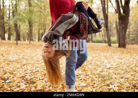 Porträt einer glücklichen Familie, die im Herbst zwischen gelben gefallenen Blättern im Park steht. Eine Frau, die ein Teenager auf dem Kopf hält. Stockfoto