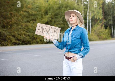 Porträt einer jungen, seriösen blonden Frau, die Pappe mit Inschrift überall aufzieht und schmal schaut. Auf Reisen. Stockfoto