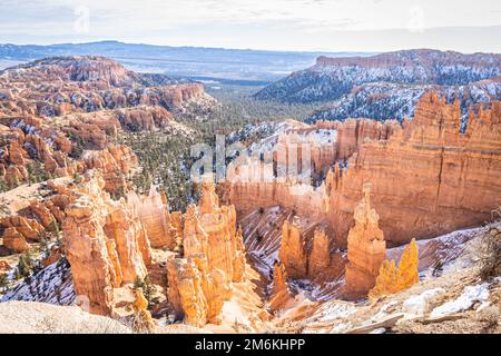 Der Bryce Canyon ist mit frisch gefallenem Schnee und fernen Bergen und leuchtend farbigen orangefarbenen Klippen geschmückt. Stockfoto