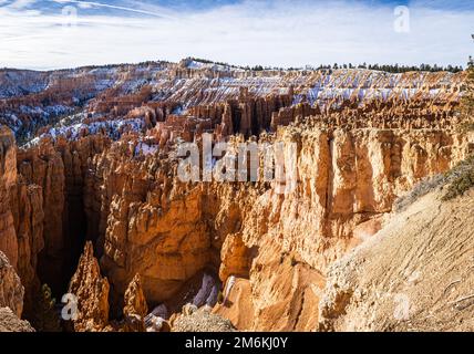 Der Bryce Canyon ist mit frisch gefallenem Schnee und fernen Bergen und leuchtend farbigen orangefarbenen Klippen geschmückt. Stockfoto