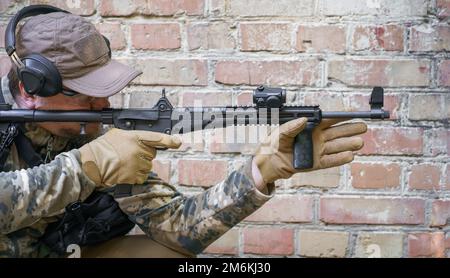 Fortbildungszyklus für Zivilpolizeitruppen im Dienst. Ein Mann mit einer Waffe steht seitlich neben einer Ziegelmauer, während fortgeschrittene Schusswaffen, Defe Stockfoto