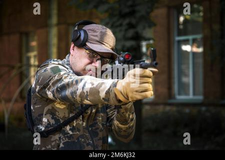 Kadett-Trainingskurs, Mann mit Waffe in Militäruniform, taktisches Gehörschutz-Headset. Ausbildung in Schießoperationen Cent Stockfoto