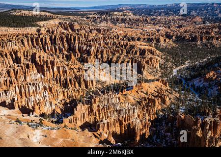 Der Bryce Canyon ist mit frisch gefallenem Schnee und fernen Bergen und leuchtend farbigen orangefarbenen Klippen geschmückt. Stockfoto