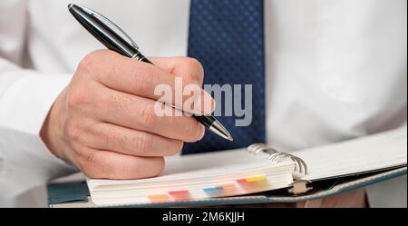Hände eines Geschäftsmannes, der einen Zeitplan schreibt oder Ideen in ein Tagebuch schreibt Stockfoto