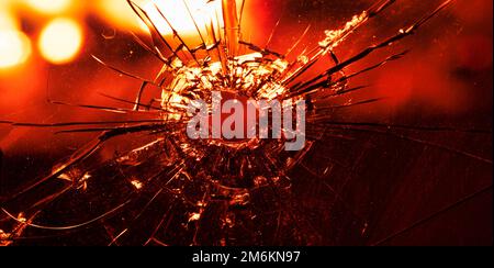 Risse im Glas, ein Einschussloch, auf einem Hintergrund von fokussierten Flammen. Abstrakter Hintergrund oder abstrakte Textur. Stockfoto