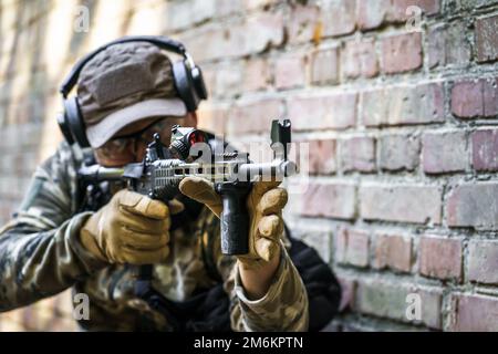 Ausbildungszyklus im Dienst für Zivilpolizeitruppen. Junger Mann mit Waffe, der bei fortgeschrittenen Schusswaffen seitlich neben einer Mauer steht Stockfoto