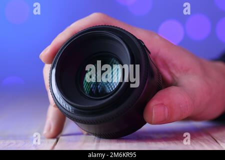 chinesisches 50mm-mm-Objektiv in der Hand auf Tisch und farbigem Hintergrund Stockfoto