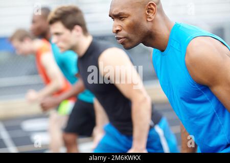 Bereit, fertig... Nahaufnahme eines männlichen Läufers in einer Reihe von anderen Athleten, die im Hintergrund verschwommen sind. Stockfoto