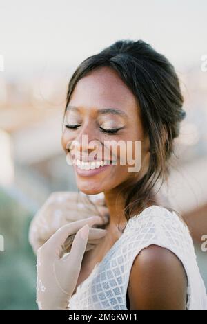 Lächelnde Braut in Handschuhen berührt ihre Schlüsselknochen mit ihren Händen. Hochformat Stockfoto