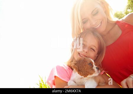 Tierbegleitung macht ein glücklicheres Zuhause. Porträt einer Mutter, Tochter und eines Welpen in der Wildnis. Stockfoto