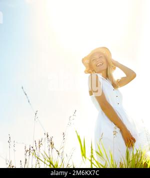 Genießen Sie die Ruhe der Natur. Eine wunderschöne, blonde Frau, die an einem warmen Sommertag auf einer Wiese steht und einen Sonnenhut trägt. Stockfoto