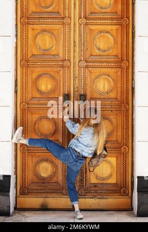 Eine Frau versucht gewaltige Holztüren mit einem klassischen Muster zu öffnen. Brechen Sie in eine verschlossene Tür ein. Stockfoto
