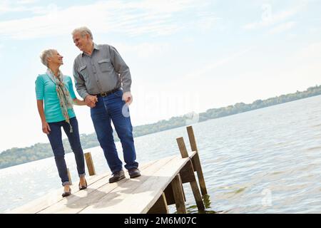 So machen wir unsere Liebe zum letzten Mal. Ein liebevolles älteres Paar, das sich ansieht, während es auf einem Steg steht. Stockfoto