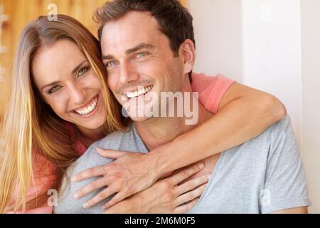 Er ist der, den ich will. Eine wunderschöne junge Frau, die ihren Mann von hinten umarmt, während sie auf der Couch sitzen. Stockfoto