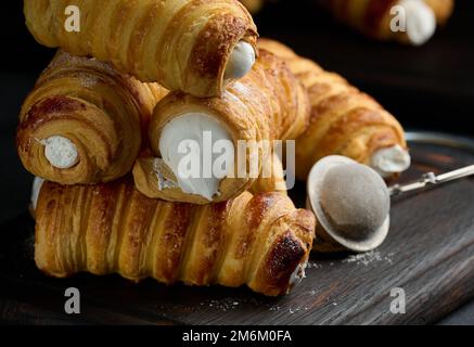 Gebackene Tubuli gefüllt mit geschlagener Eiweiß-Creme auf einem schwarzen Küchenbrett aus Holz Stockfoto